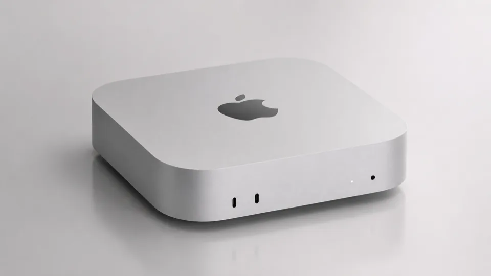 光沢のある白い背景に置かれたシルバーのMac mini本体。上面中央にはAppleのロゴがあり、前面には2つの小さな黒いポートと2つの白いインジケーターライトがある。